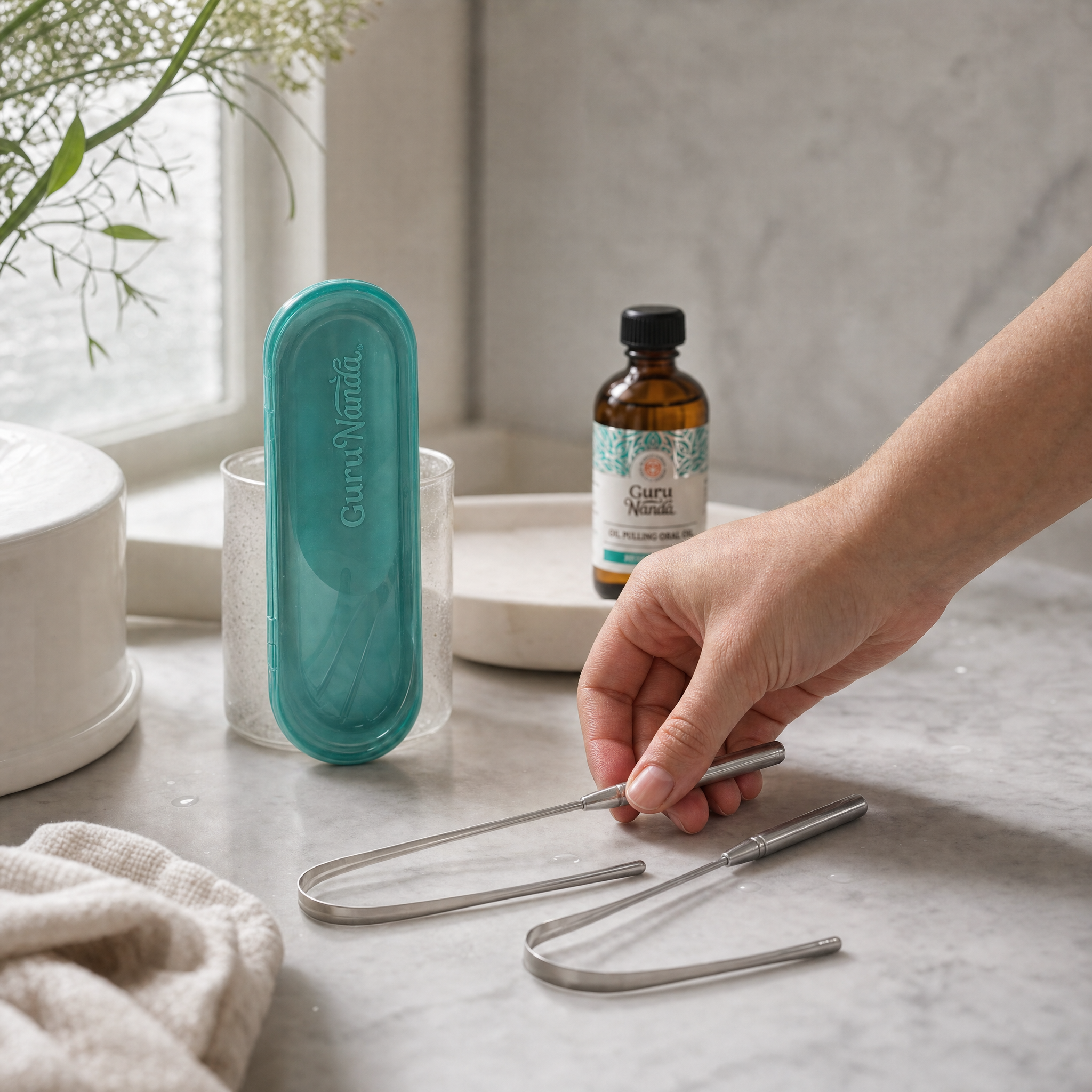 Two stainless steel tongue scrapers and a teal travel case on a marble counter
